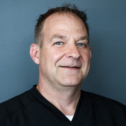 Headshot of Dr. Psota, chiropractor in South Overland Park, featuring a blue background and black scrubs