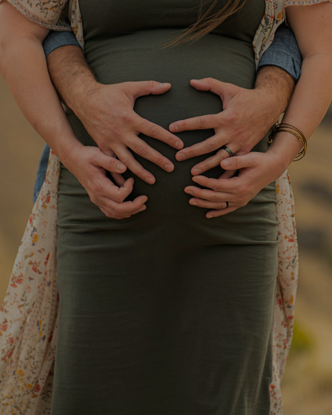 A couple embraces, with their hands forming a heart shape over a pregnant woman's belly.
