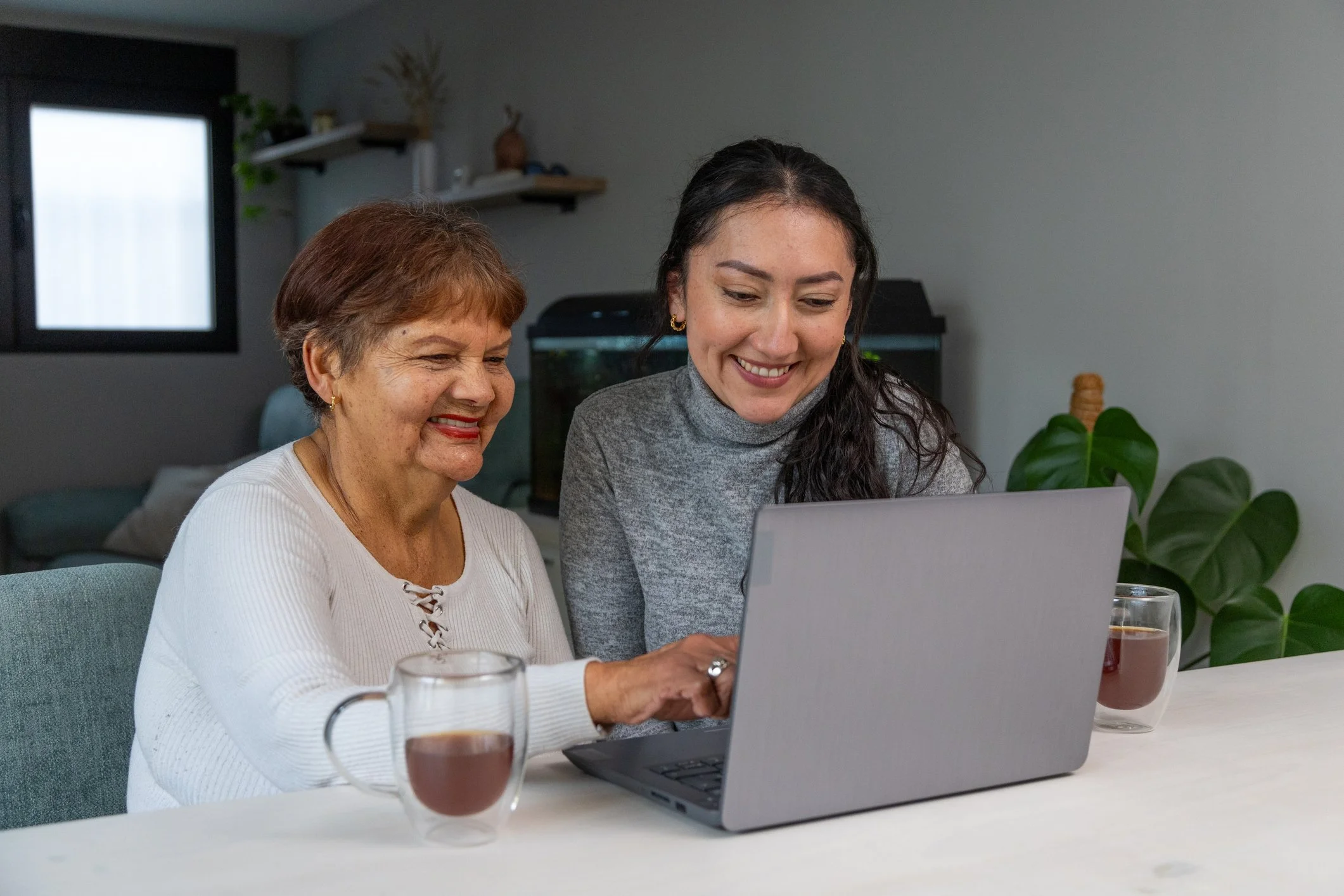A Digital Navigator helps an older woman use a laptop at home.