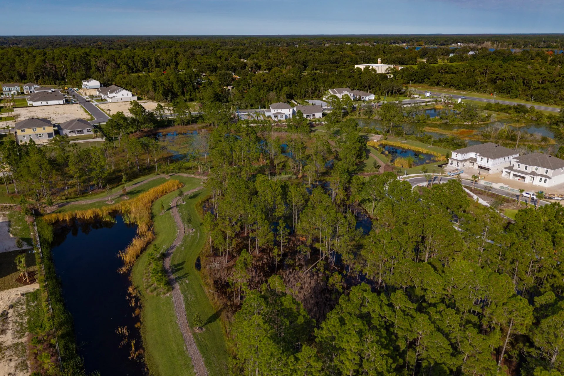 Aerial view of a suburban area with houses, water bodies, and green trees, adjacent to a highway.