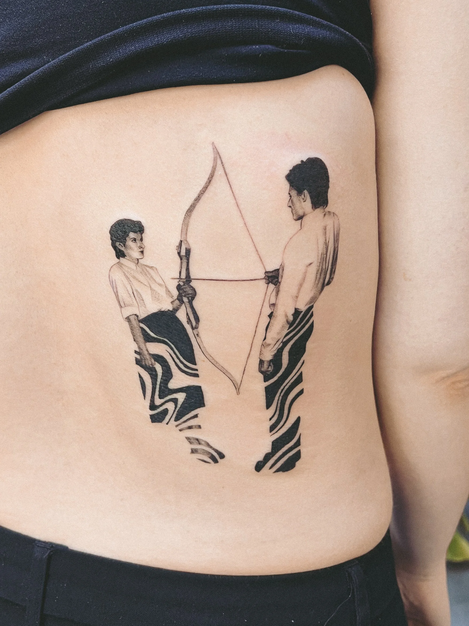 Tattoo of two men in a face-to-face stance, one holding a bow and arrow, on person's side ribcage. marina abramovic tattoo
