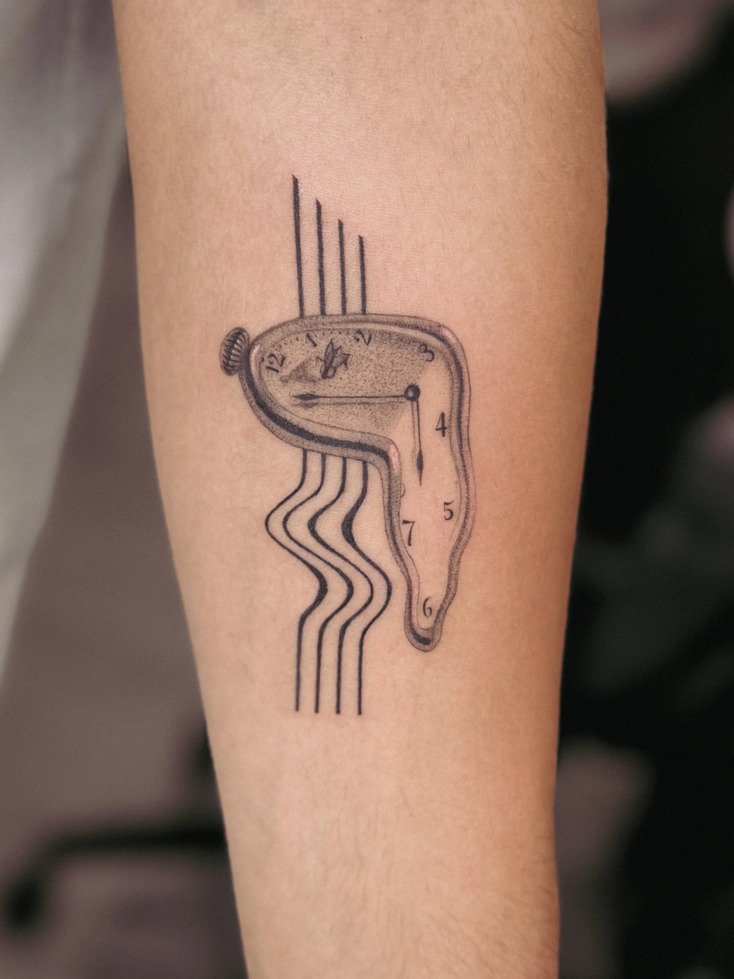 Tattoo of a melting clock with distorted numbers on a person's arm. dali clock time tattoo abstract