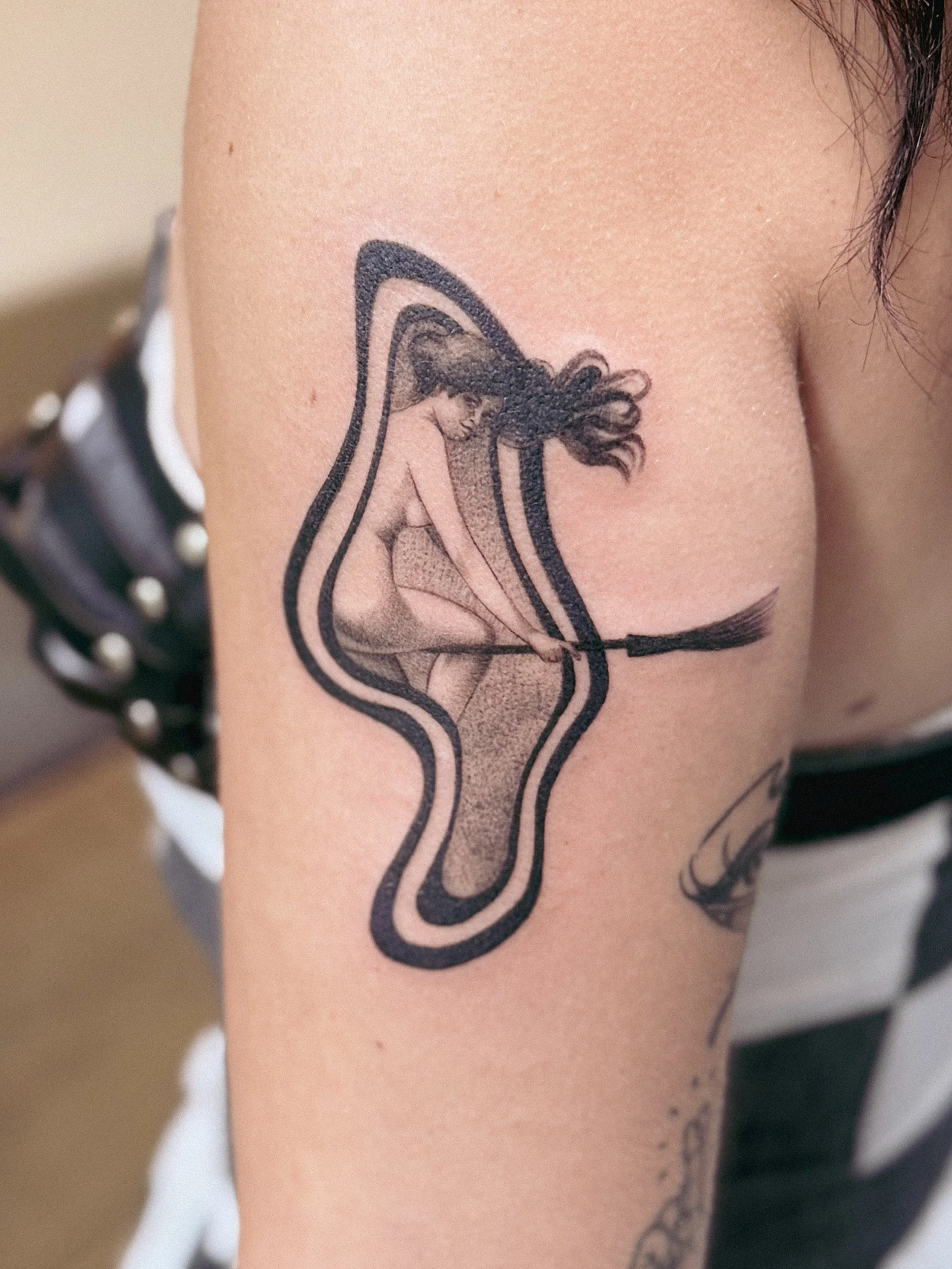Close-up of a tattoo of a woman with flowing hair, sitting and leaning forward on a person's upper arm. witch tattoo abstract witchy