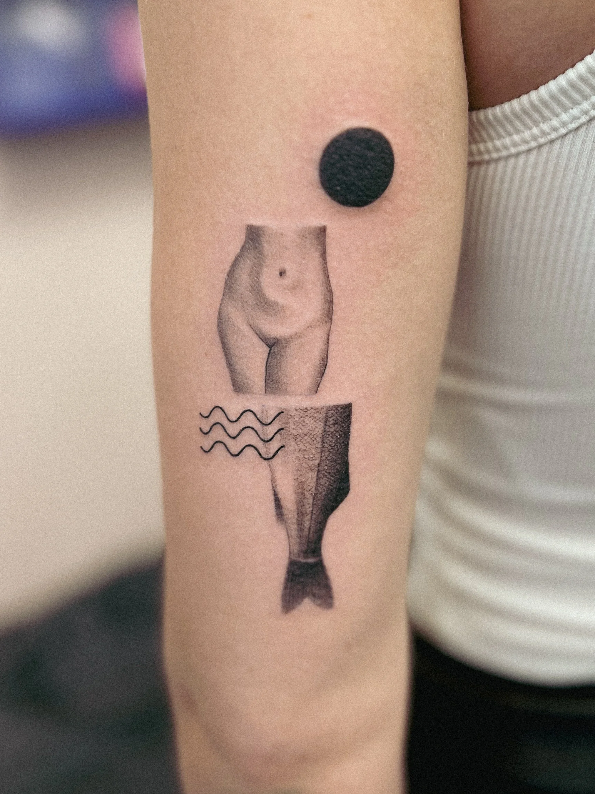 Tattoo of a female torso and legs with waves, a black dot, and a photo of a waist with a navel. mermaid tattoo