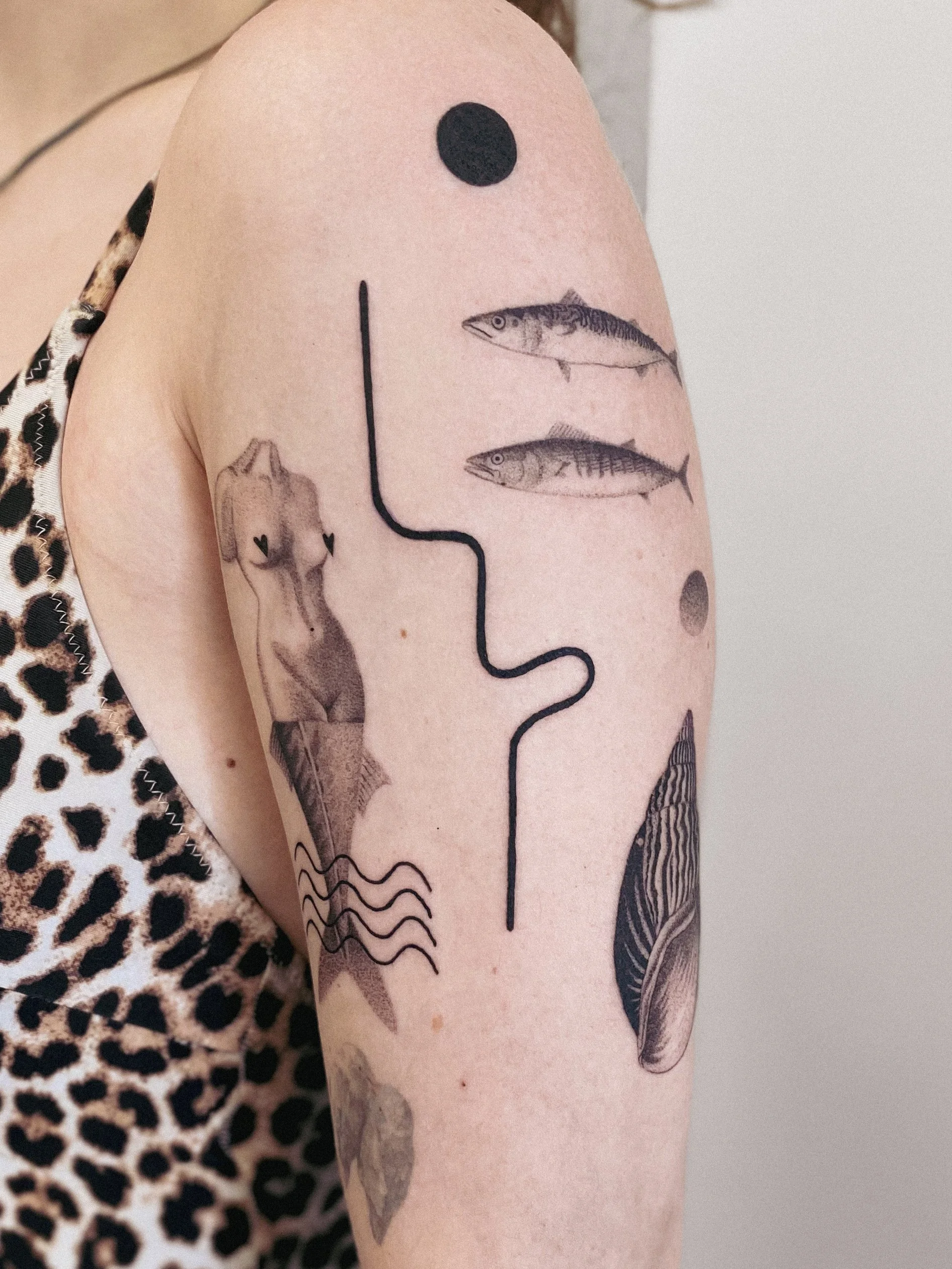 Tattoo on person's arm featuring a pig, a propeller, two fish, and a black dot.