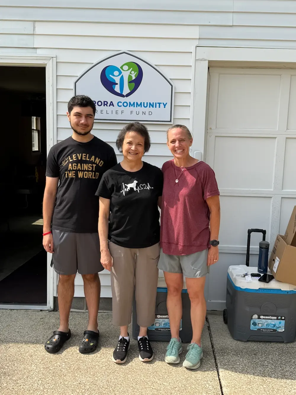 Three people standing outside in front of a sign that reads 'Aurora Community Relief Fund.'