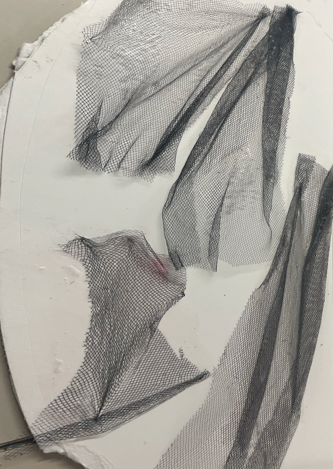 A piece of paper with black mesh fabric draped over it, creating abstract shapes and shadows.