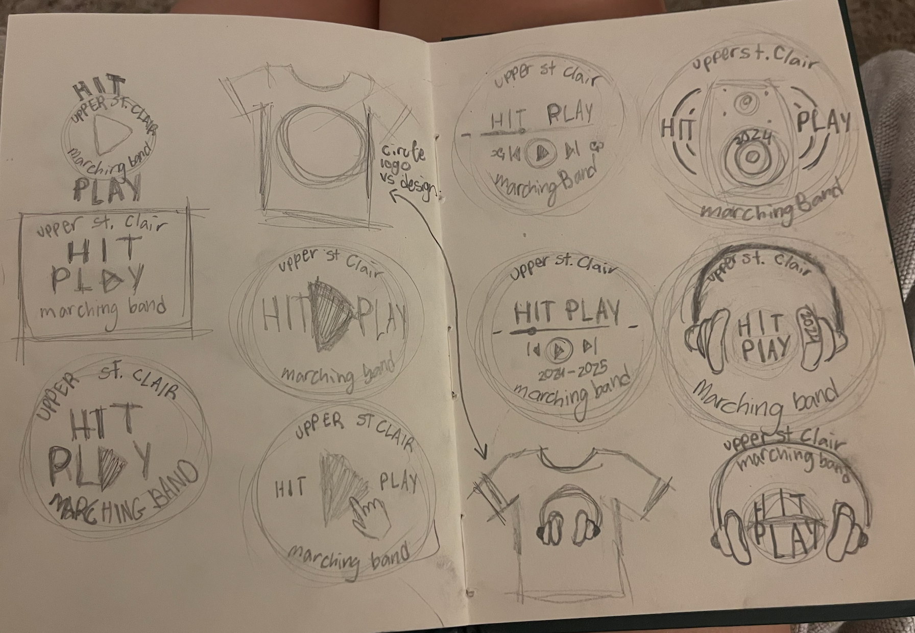 Sketches of circular logos and designs for 'Upper St Clair HIT Play,' a marching band, with variations including play buttons, speaker icons, a shirt outline, and a person wearing headphones, all with handwritten notes and annotations.