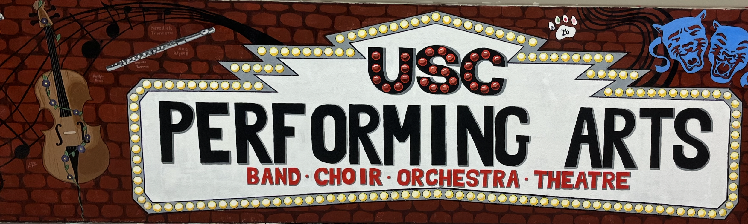 Marquee sign for USC Performing Arts featuring a guitar, a flute, and comedy/tragedy masks with a brick wall background.
