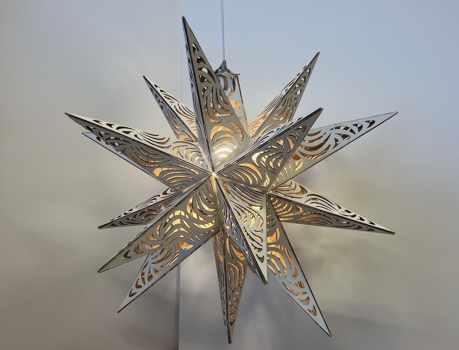 Decorative star-shaped lantern with intricate cut-out patterns, illuminated from within, hanging against a plain background.