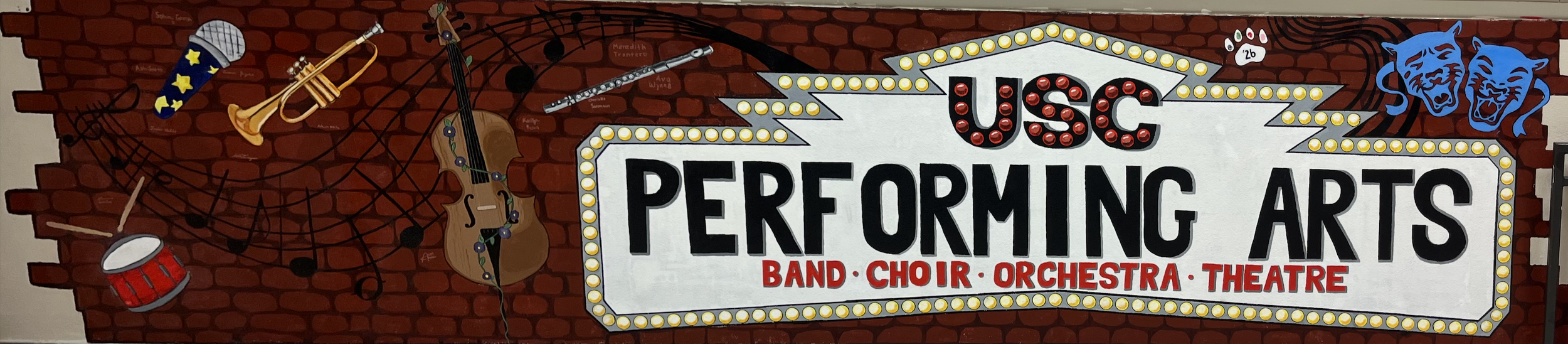 A mural on a brick wall promoting the USC Performing Arts, including band, choir, orchestra, and theatre, with musical instruments, musical notes, and theatrical masks.