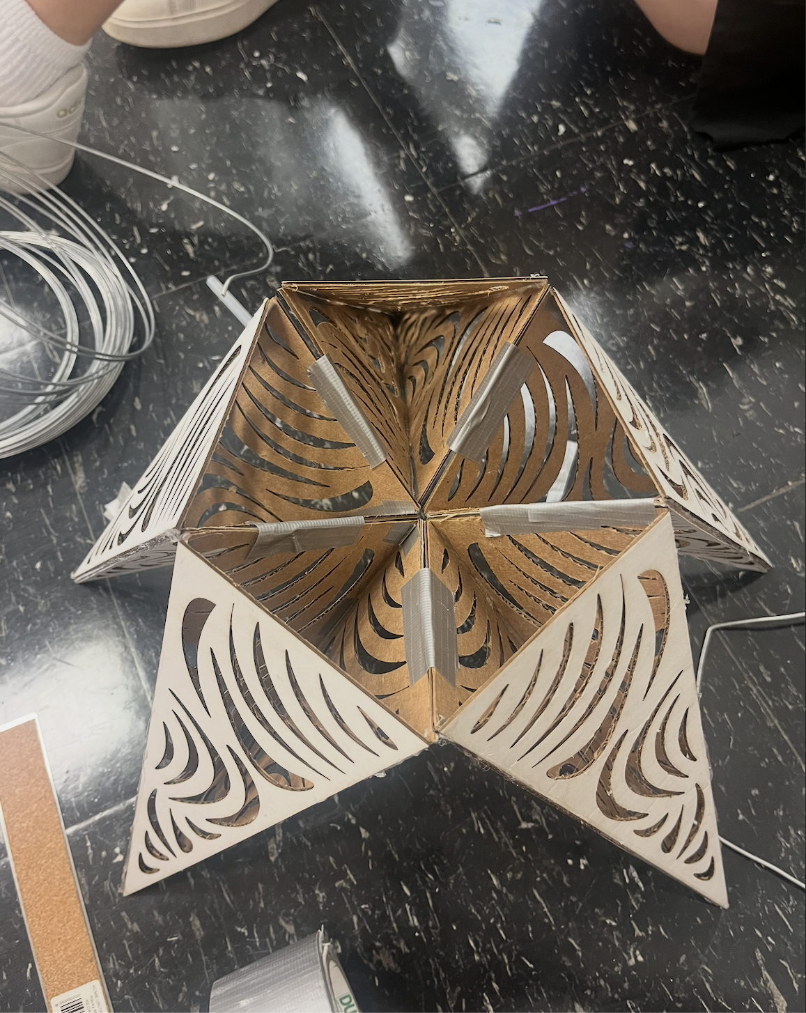 A decorative lamp with intricate laser-cut patterns, assembled in a star shape, on a black marble surface.