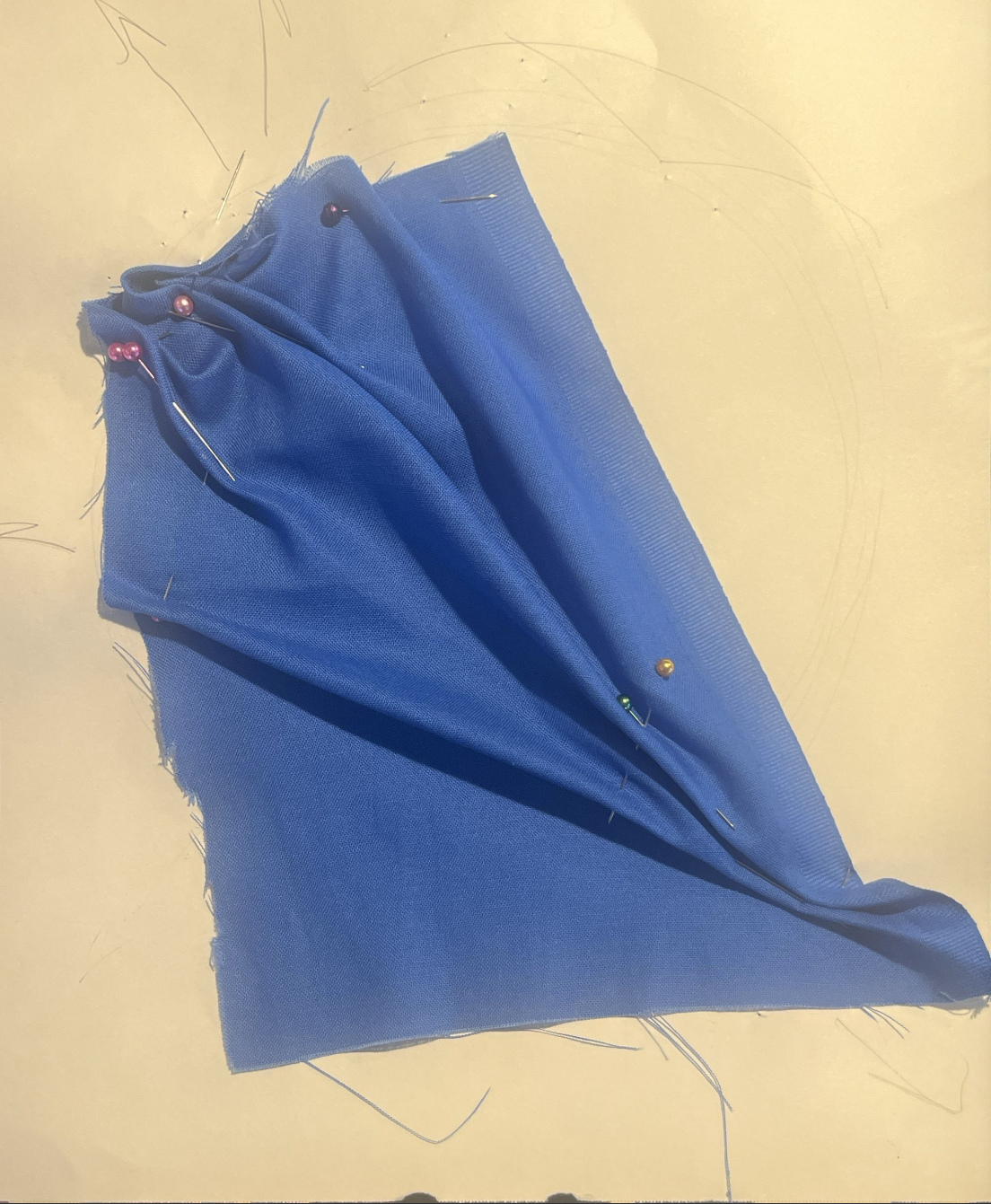 A piece of blue fabric pinned together with multicolored sewing pins on a yellow surface.