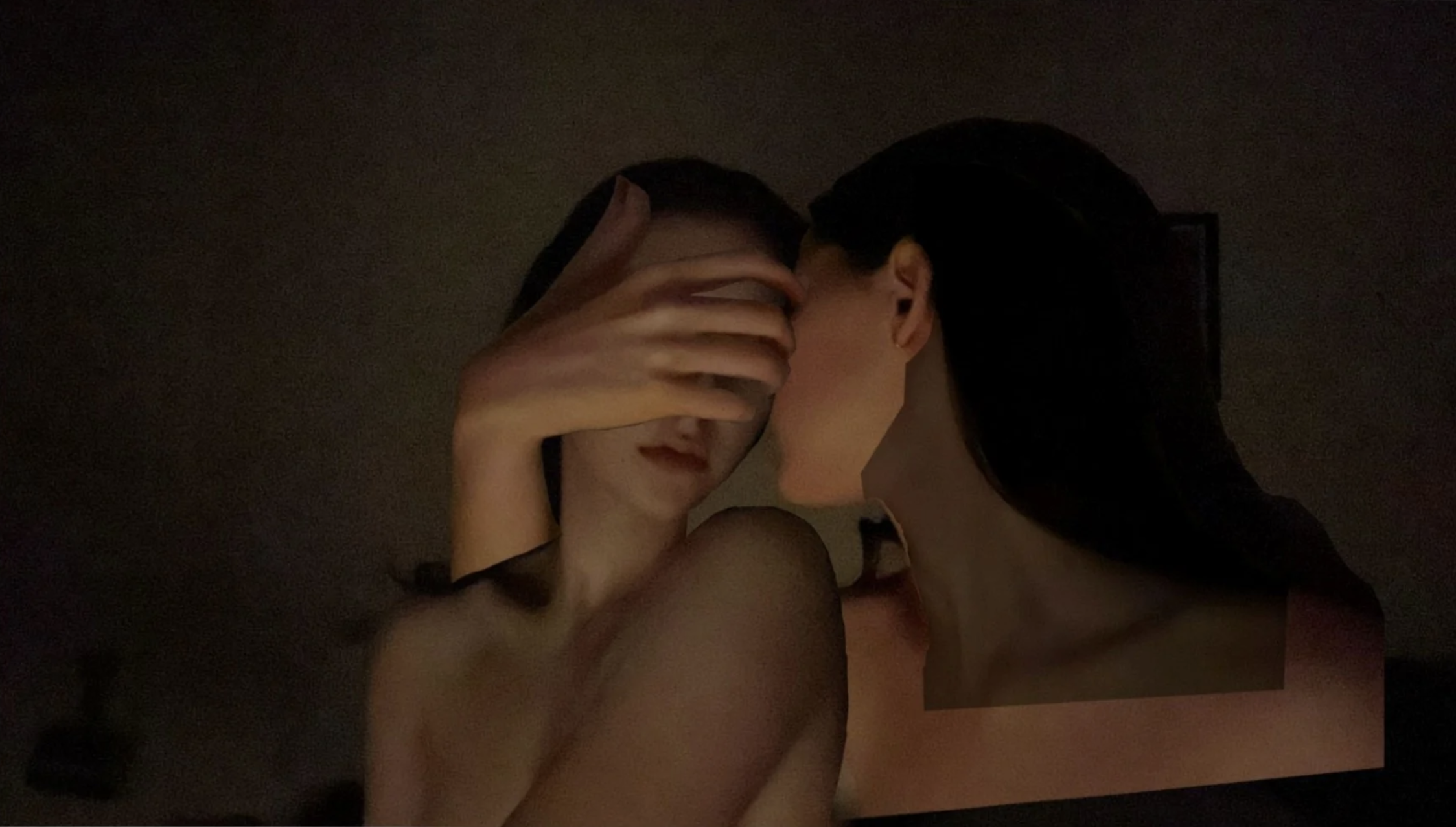 Two people in an intimate pose, close together, with one person's face partially obscured and the other's face visible, in a dimly lit setting.