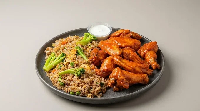 Black plate with fried rice, broccoli, chicken wings, and a small cup of white dipping sauce
