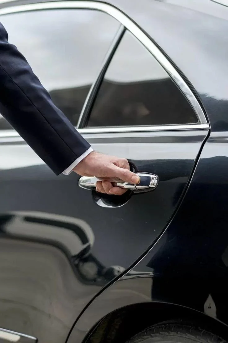 Person in a dark suit is opening the door of a black car.