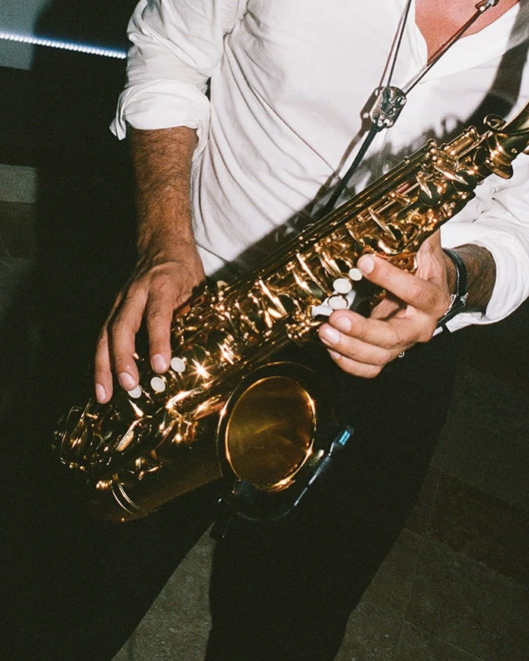 Person playing a shiny, golden saxophone while wearing a white shirt and black pants.