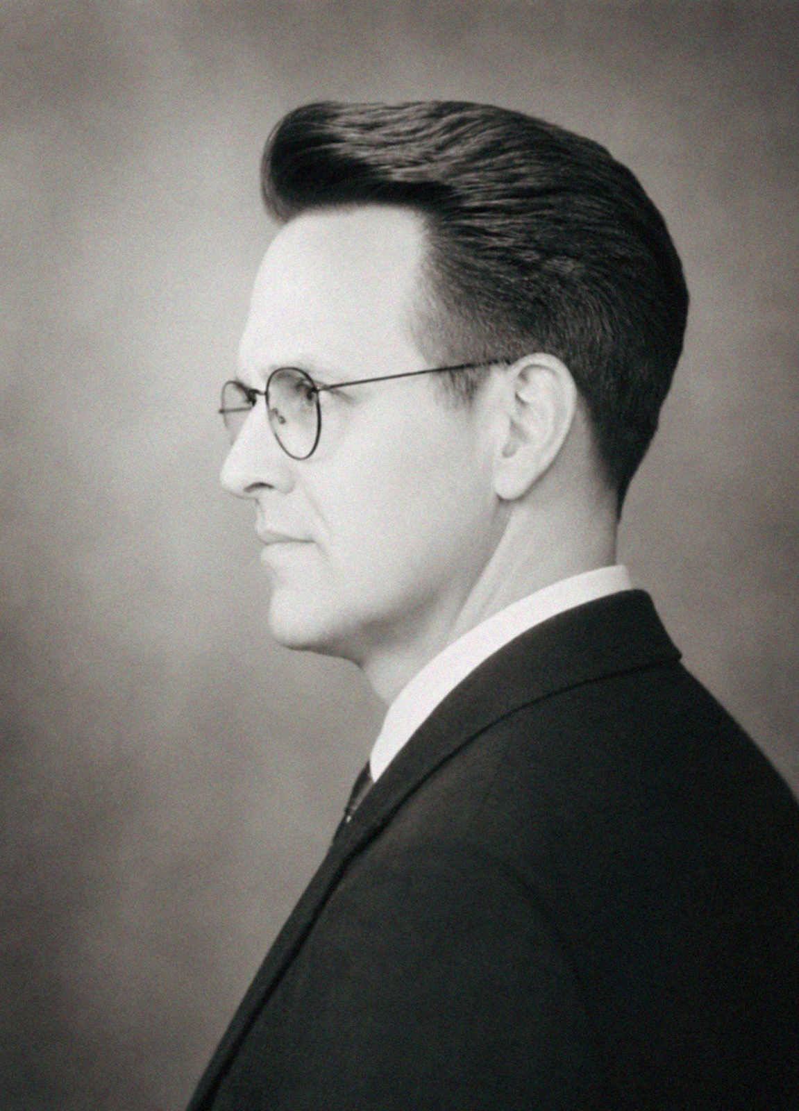 Black-and-white portrait of a woman with a slicked-back hairstyle, wearing glasses and a suit, looking to the side.