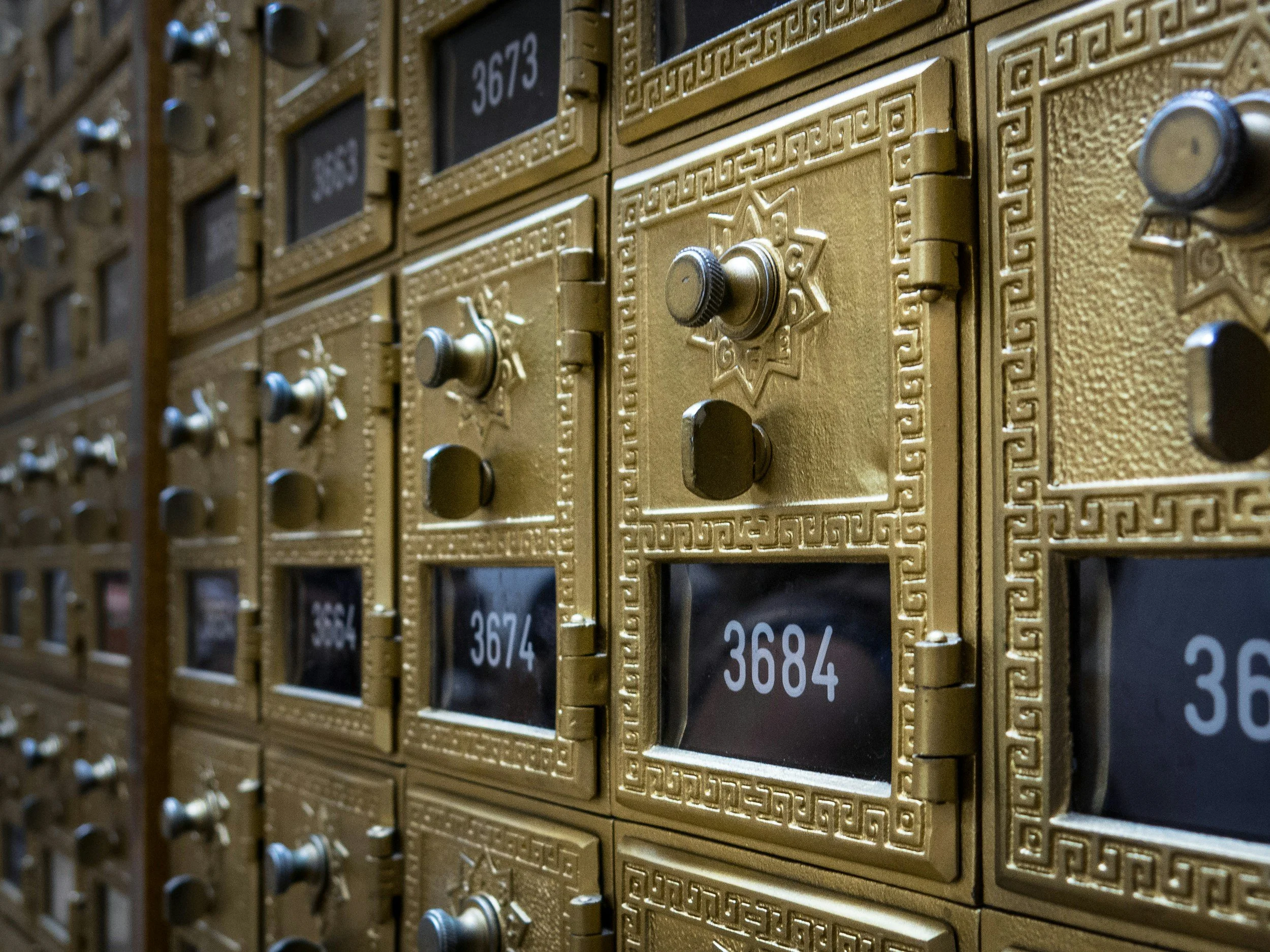 Close-up view of a vintage gold-colored postal locker with numbered compartments and small metal knobs.