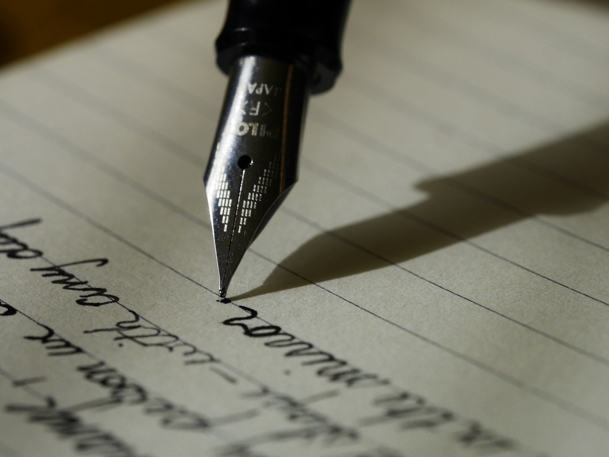 Close-up of a pen writing handwritten text on lined paper.