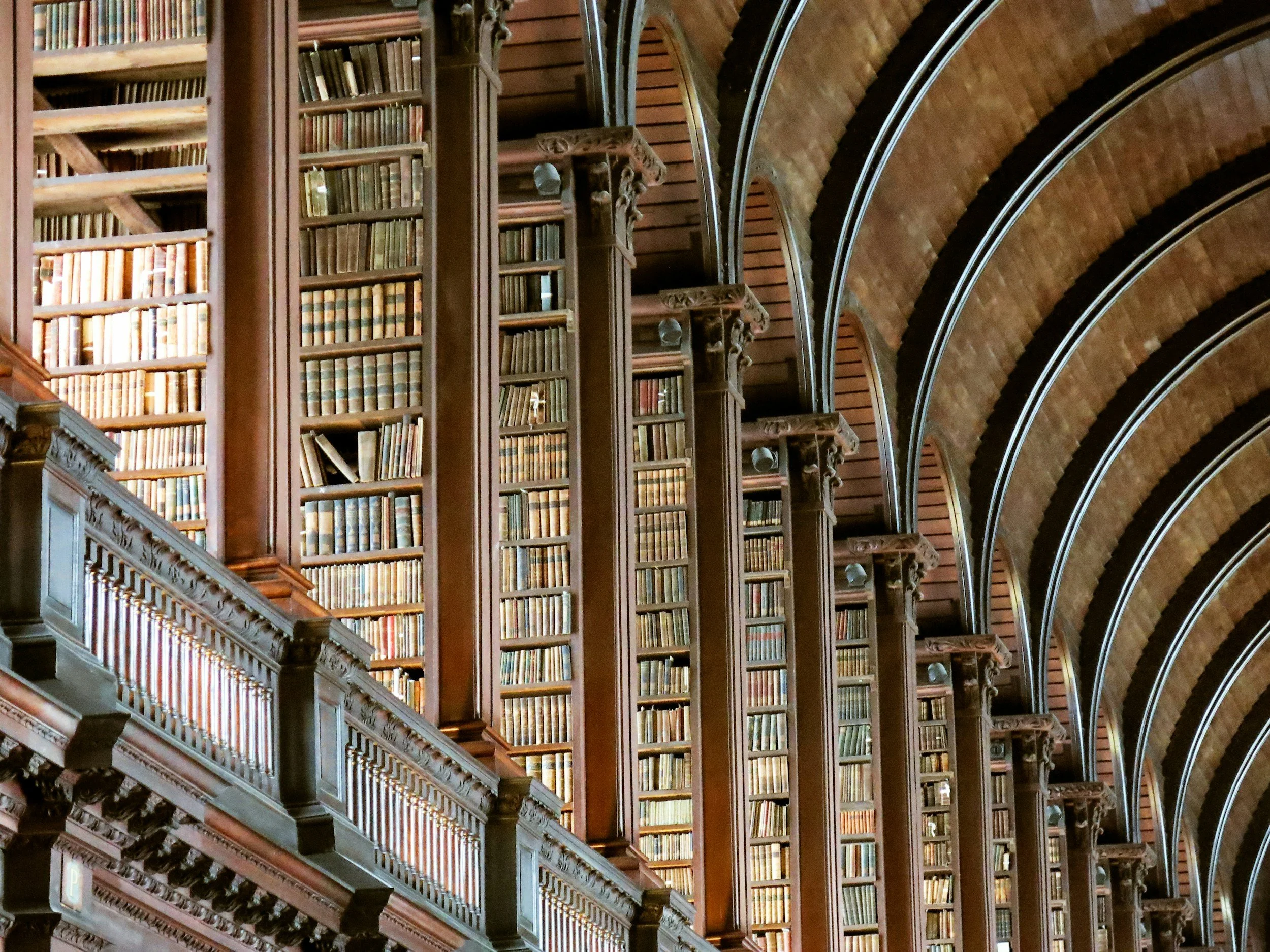 Multiple tall wooden bookshelves filled with old books in a grand historic library with arched brick ceilings.