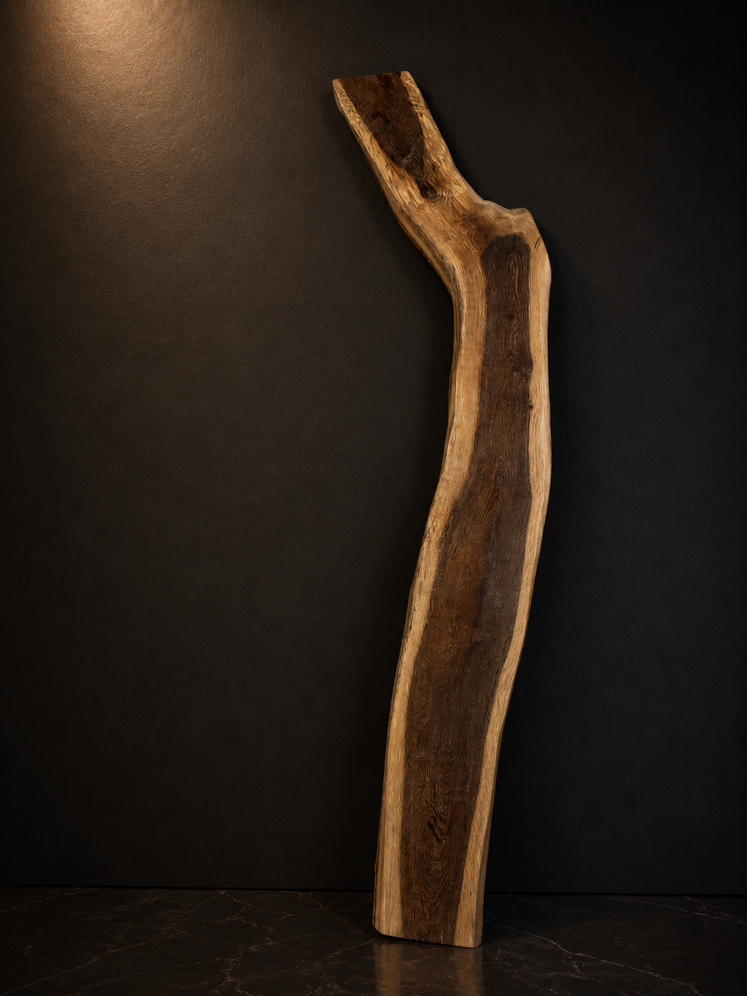 A tall, irregularly shaped wooden sculpture standing against a dark wall.
