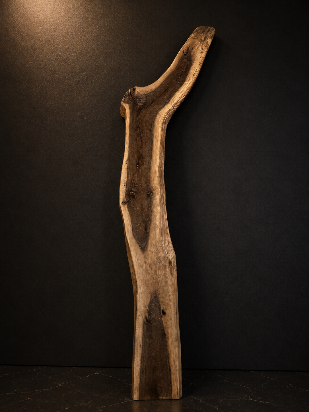 A tall wooden sculpture, curved and polished, positioned against a black background.