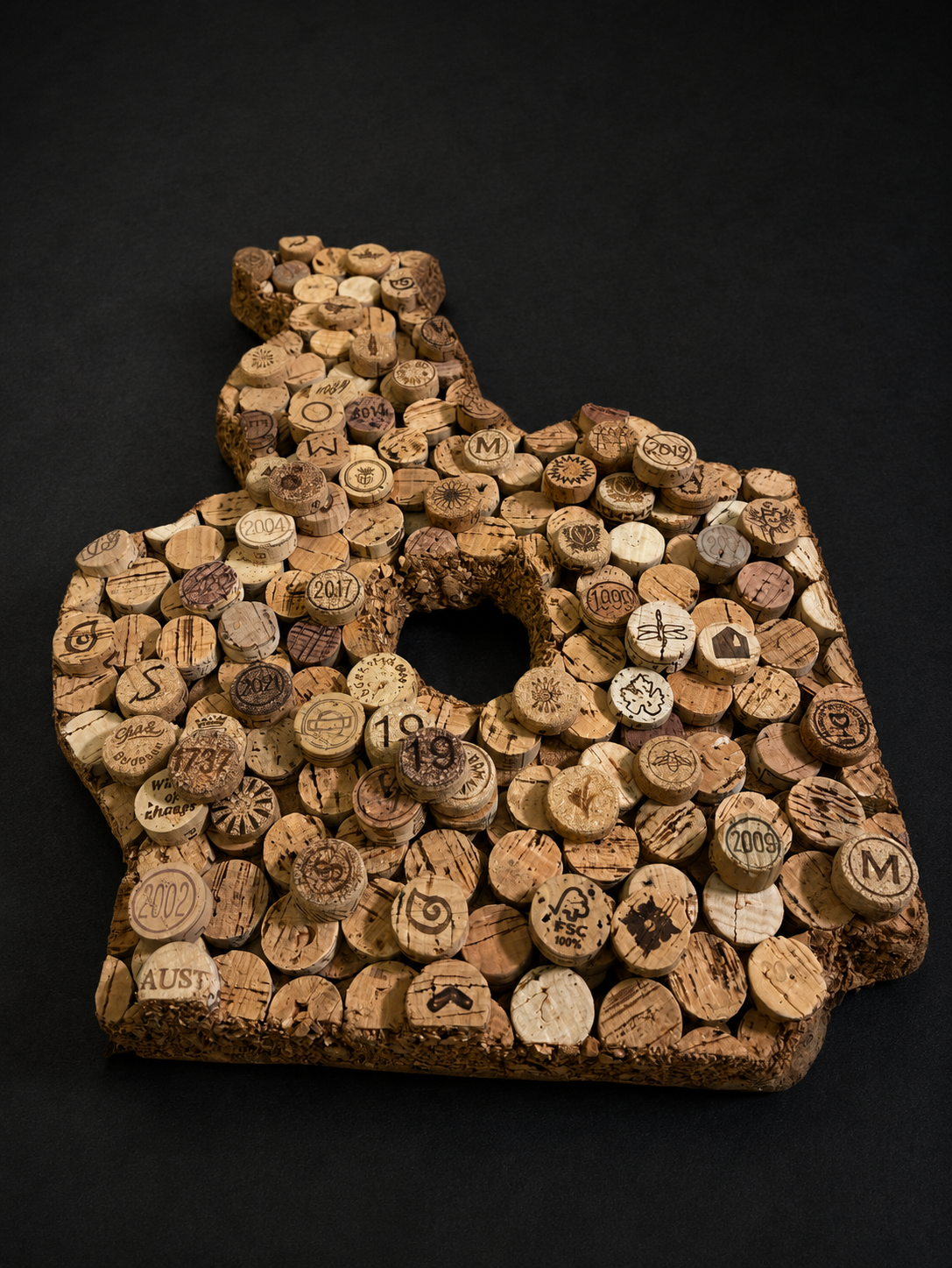 An outline of the state of Texas made from corks with engraved designs and dates, placed on a black background.