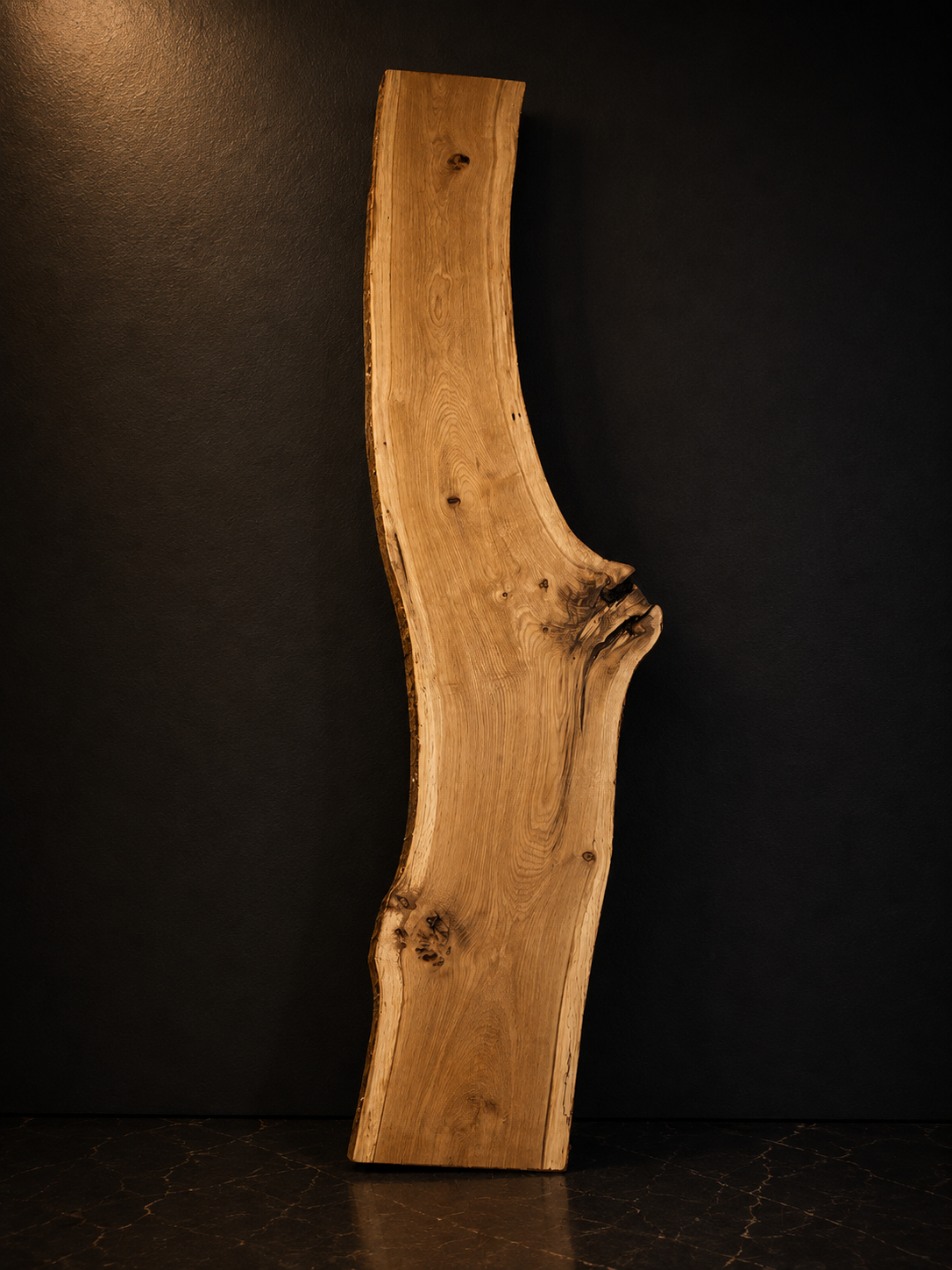 A large, curved, natural wood slab with knots and grains, standing upright against a black background.