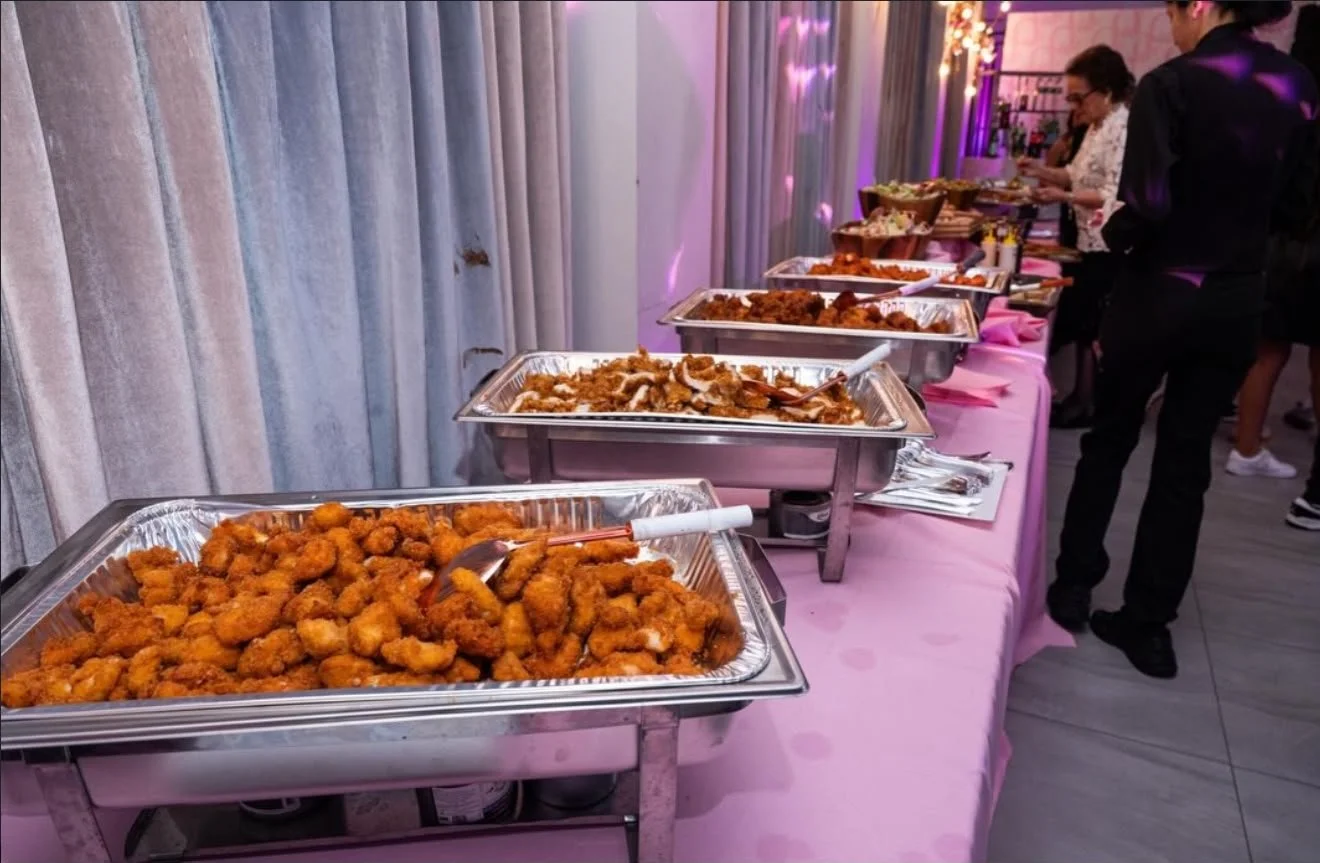 Buffet table with trays of fried chicken, other dishes, and people serving themselves at an event.