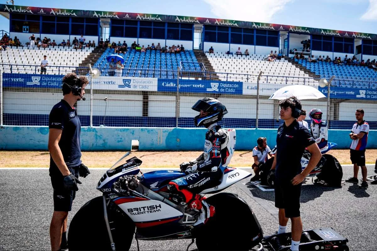 Moto racing team preparing on the grid at a race track with empty grandstands and team members gathered around the bike.
