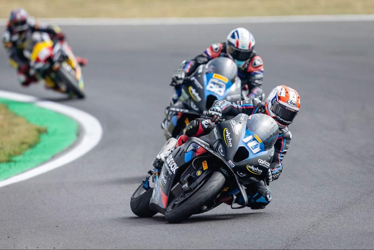 Three motorcyclists racing on a track, leaning into a turn, with one rider in front and two following closely behind.