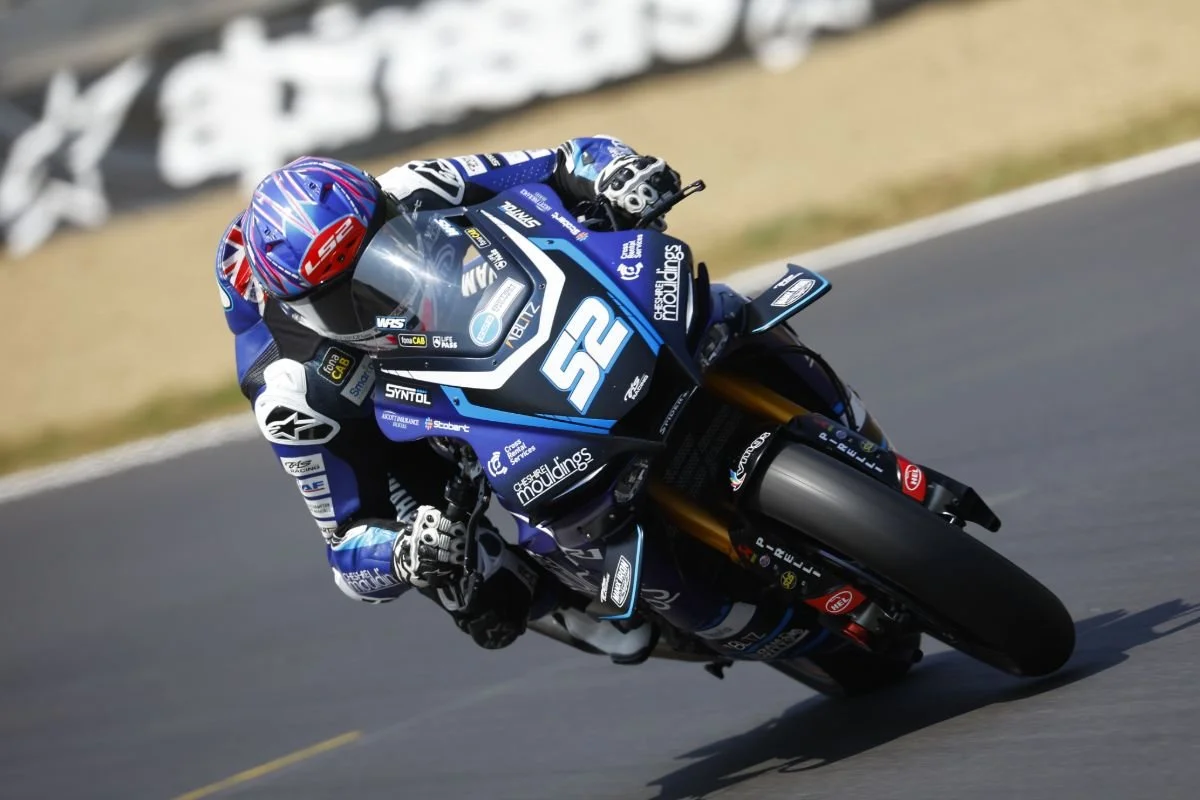Motorcycle racer in blue and black gear leaning into a turn on a racetrack.