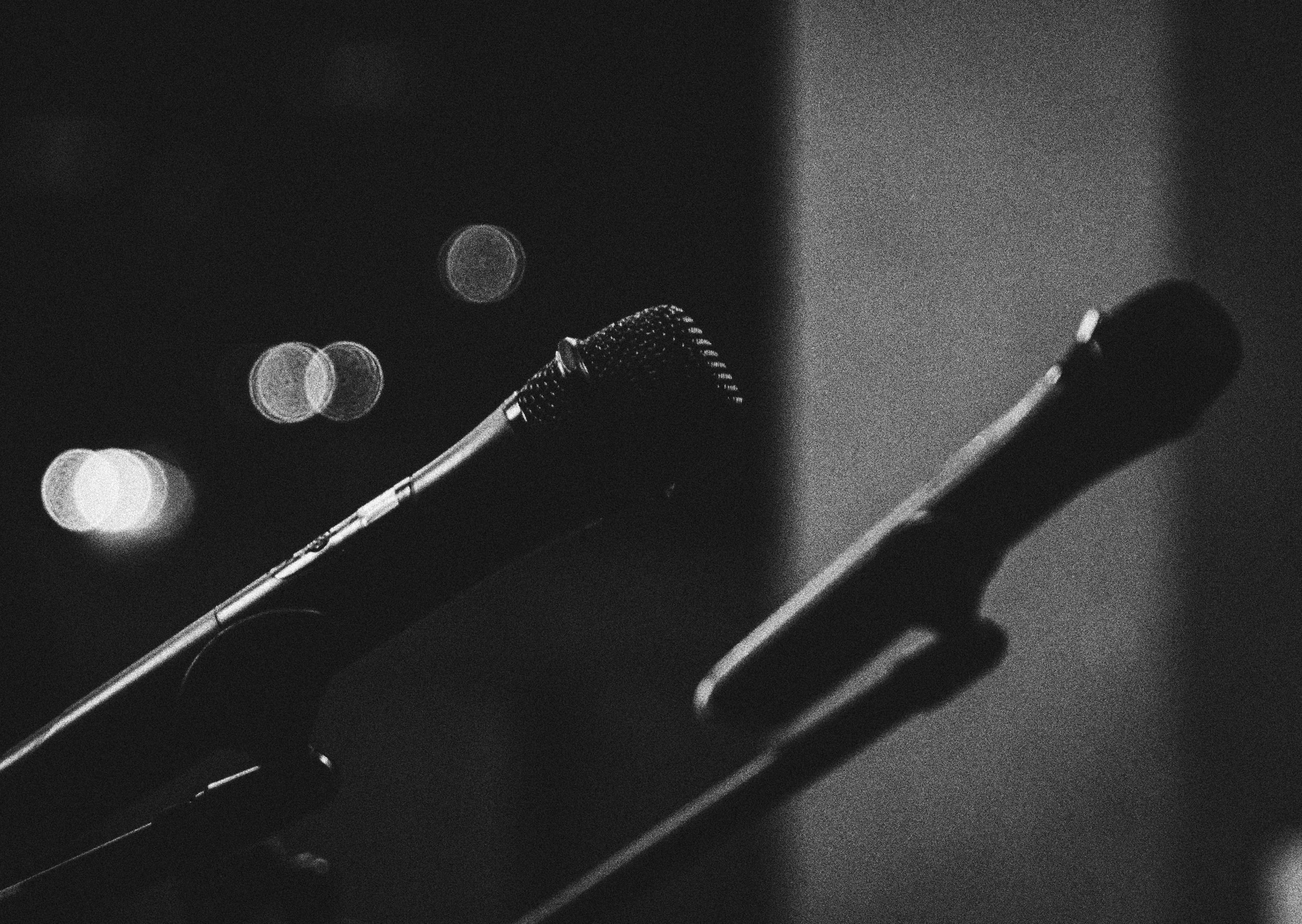 A black and white photo of a microphone on a stand with blurred city lights in the background.