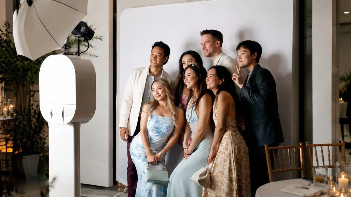 Group of seven people taking a photo in front of a white backdrop at a formal event, with a professional camera and lighting equipment visible.