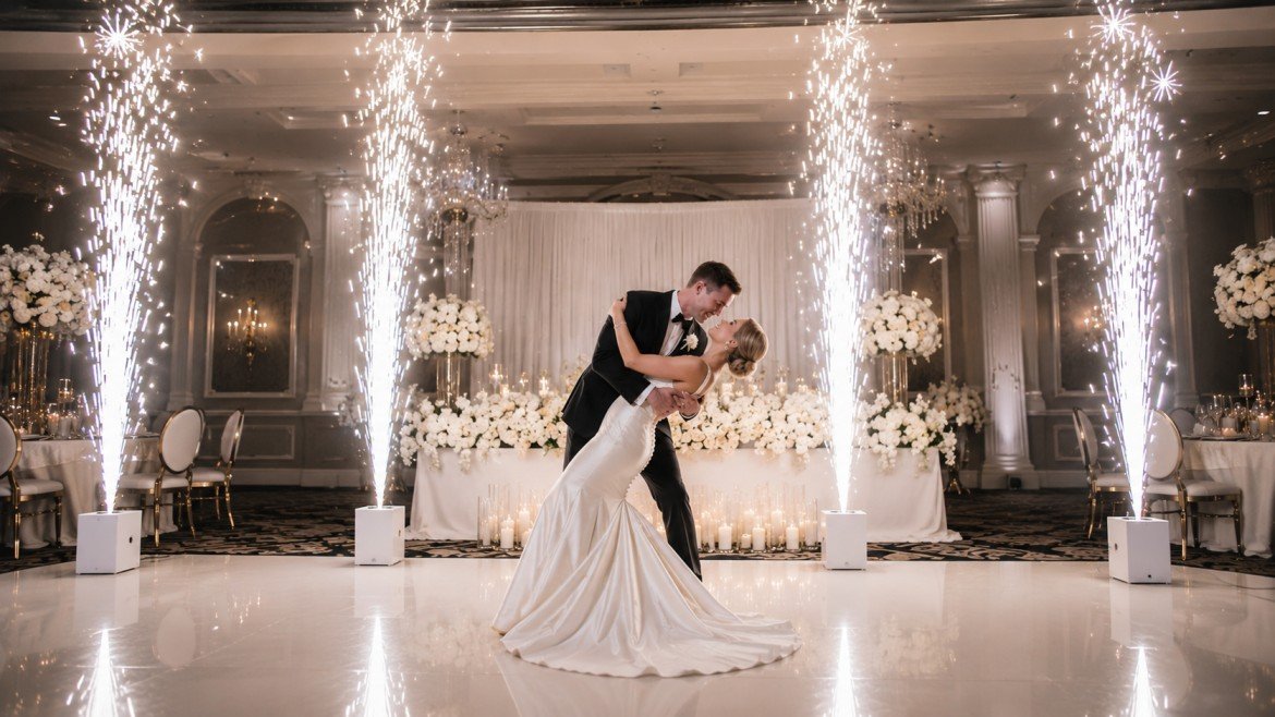 A bride and groom dancing at their wedding reception, with sparklers and flowers in the background.