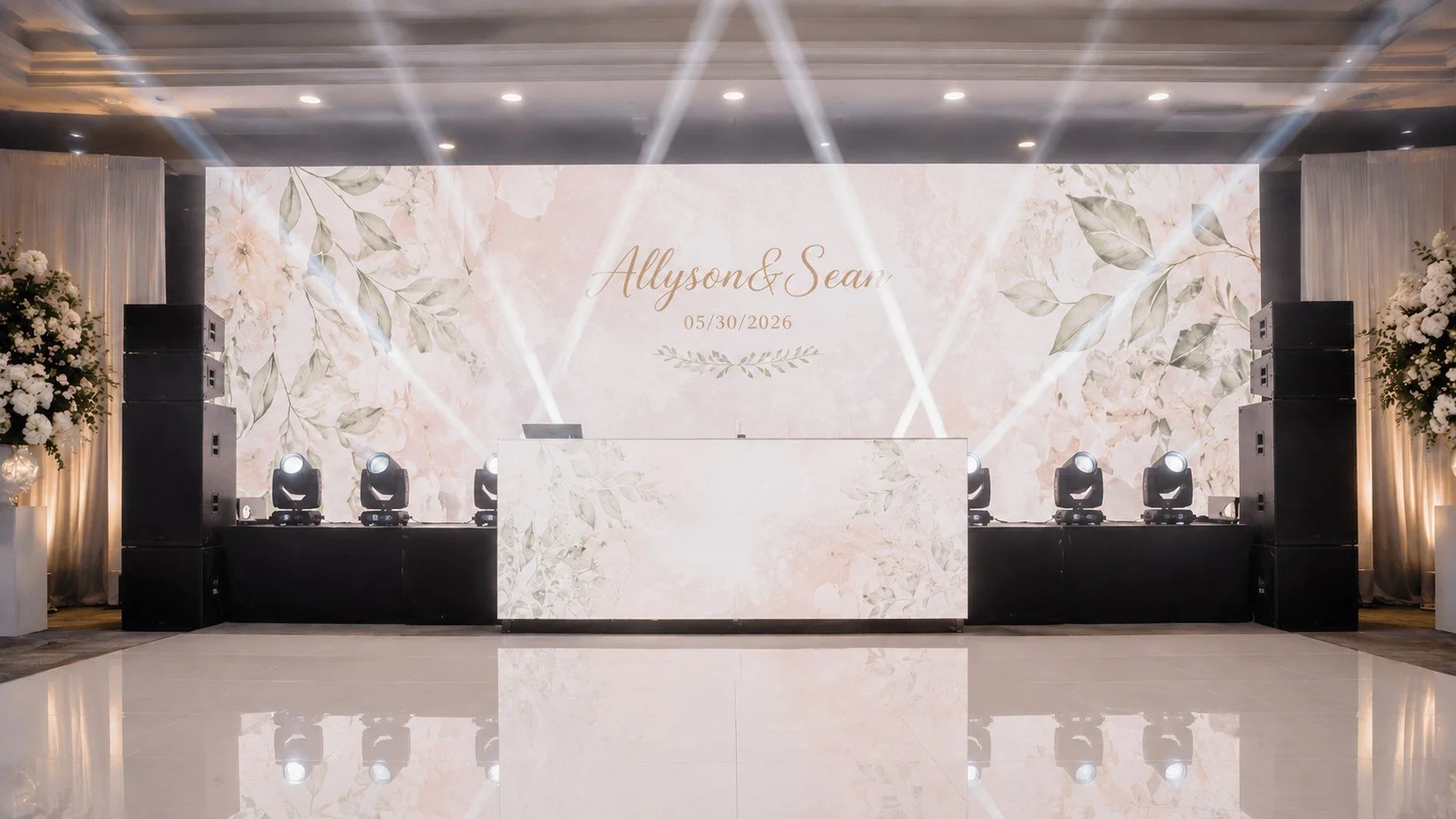 Wedding reception stage with floral-themed backdrop displaying the names Alli and Sean and the date 05/30/2026. The stage has black sound equipment and lighting, flanked by large floral arrangements on tall stands.