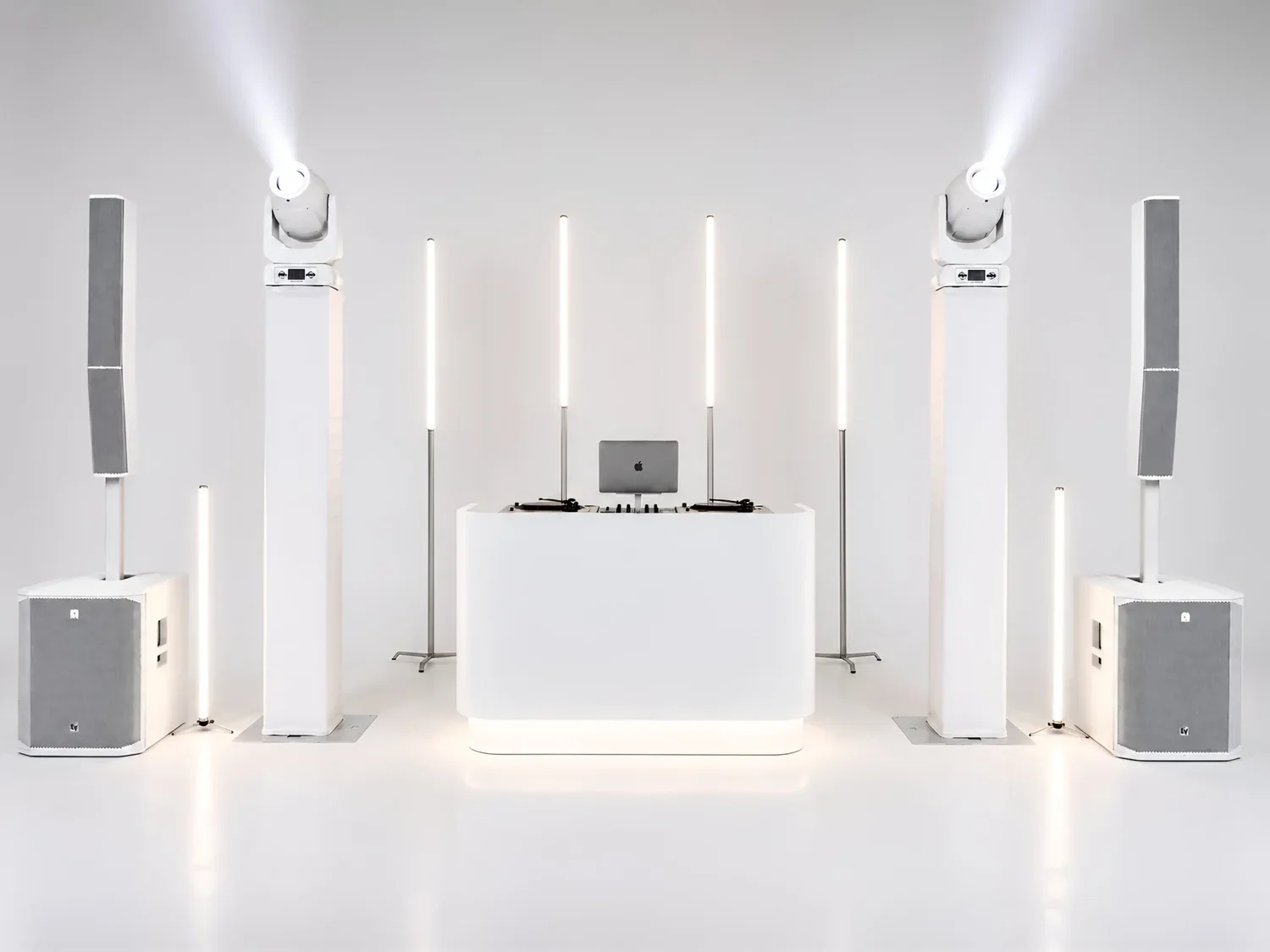 Minimalist DJ setup with speakers, LED lights, and a computer in a white room.