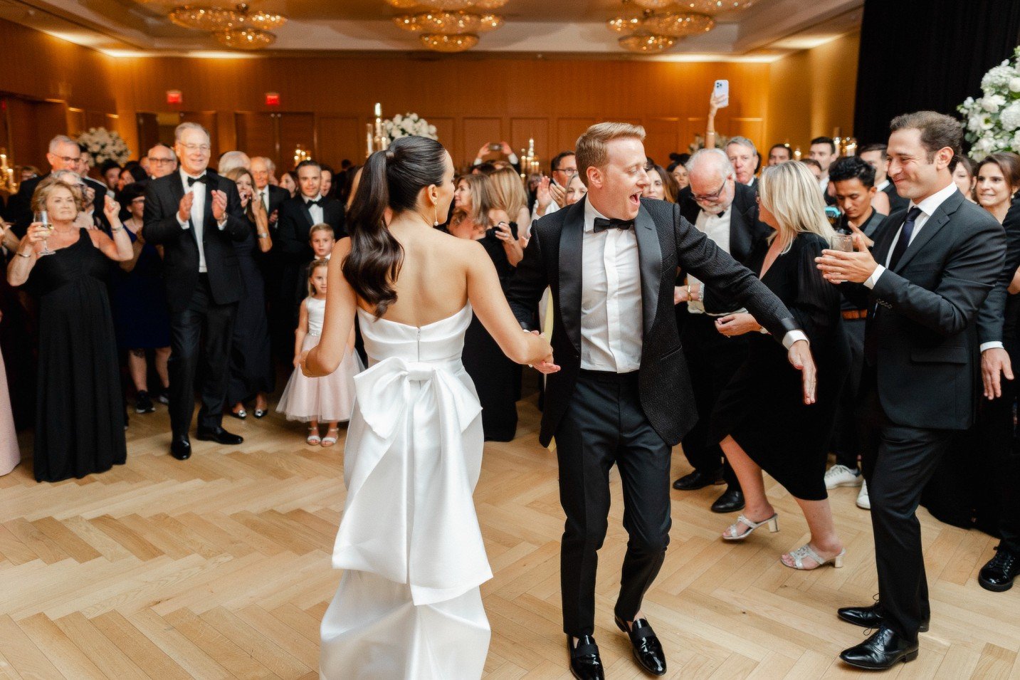 A wedding reception with a bride and groom dancing together, surrounded by guests clapping and celebrating in an elegant ballroom.