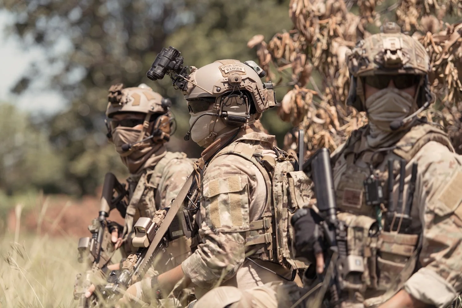 Three soldiers in camouflage uniforms and tactical gear sitting outdoors.