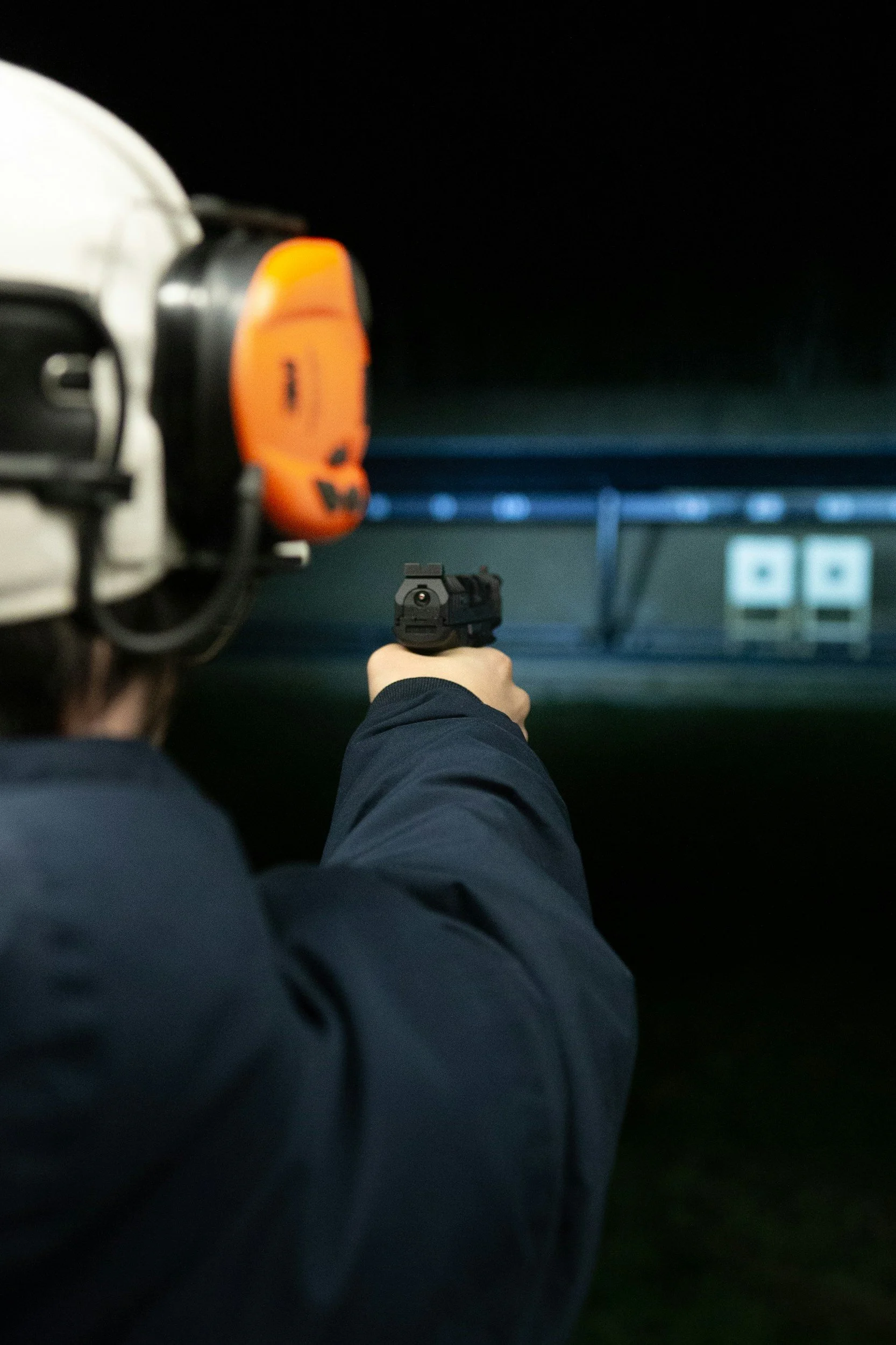 A person holding a handgun, aiming at targets in a dark shooting range.