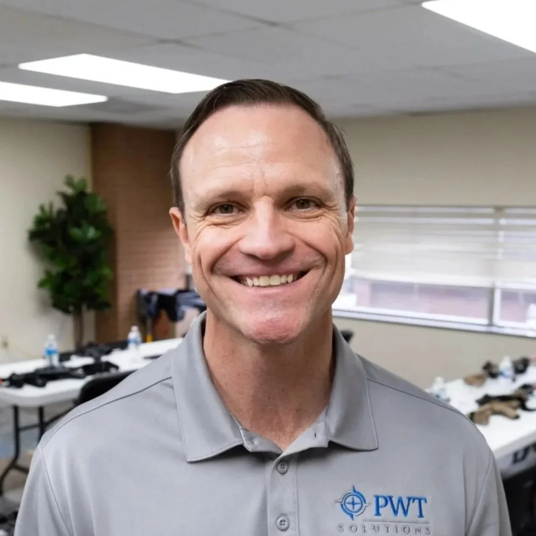 A man smiling in an office setting wearing a gray polo shirt with a PWT Solutions logo.