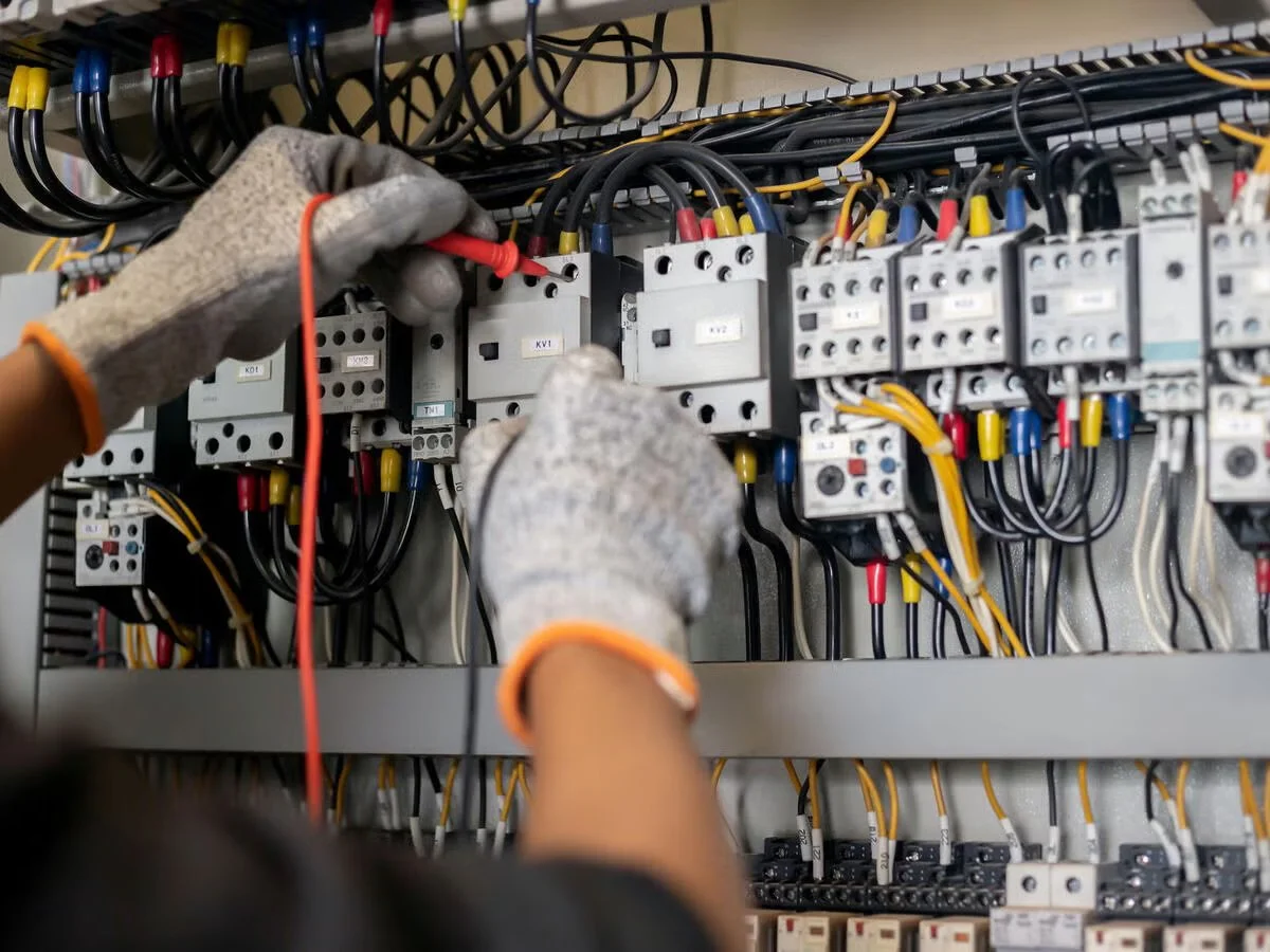 Worker wearing gloves working on electrical circuit breaker panel, connecting wires.