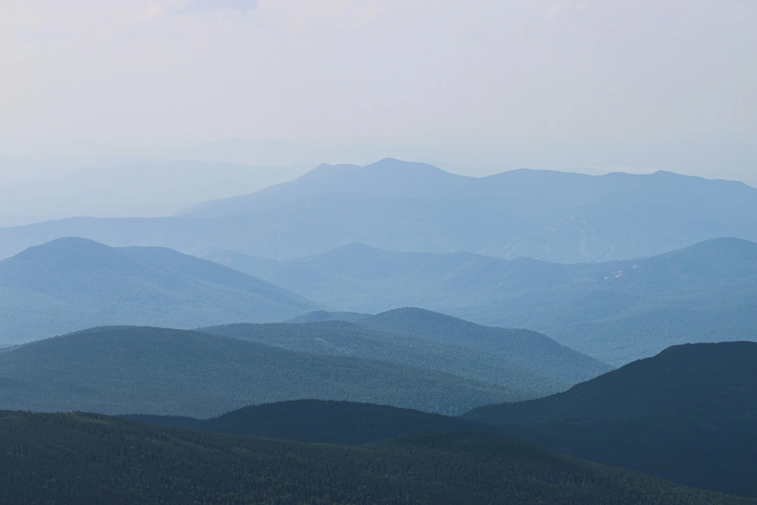 Layered mountain ranges under a cloudy sky, with blue and green hues.