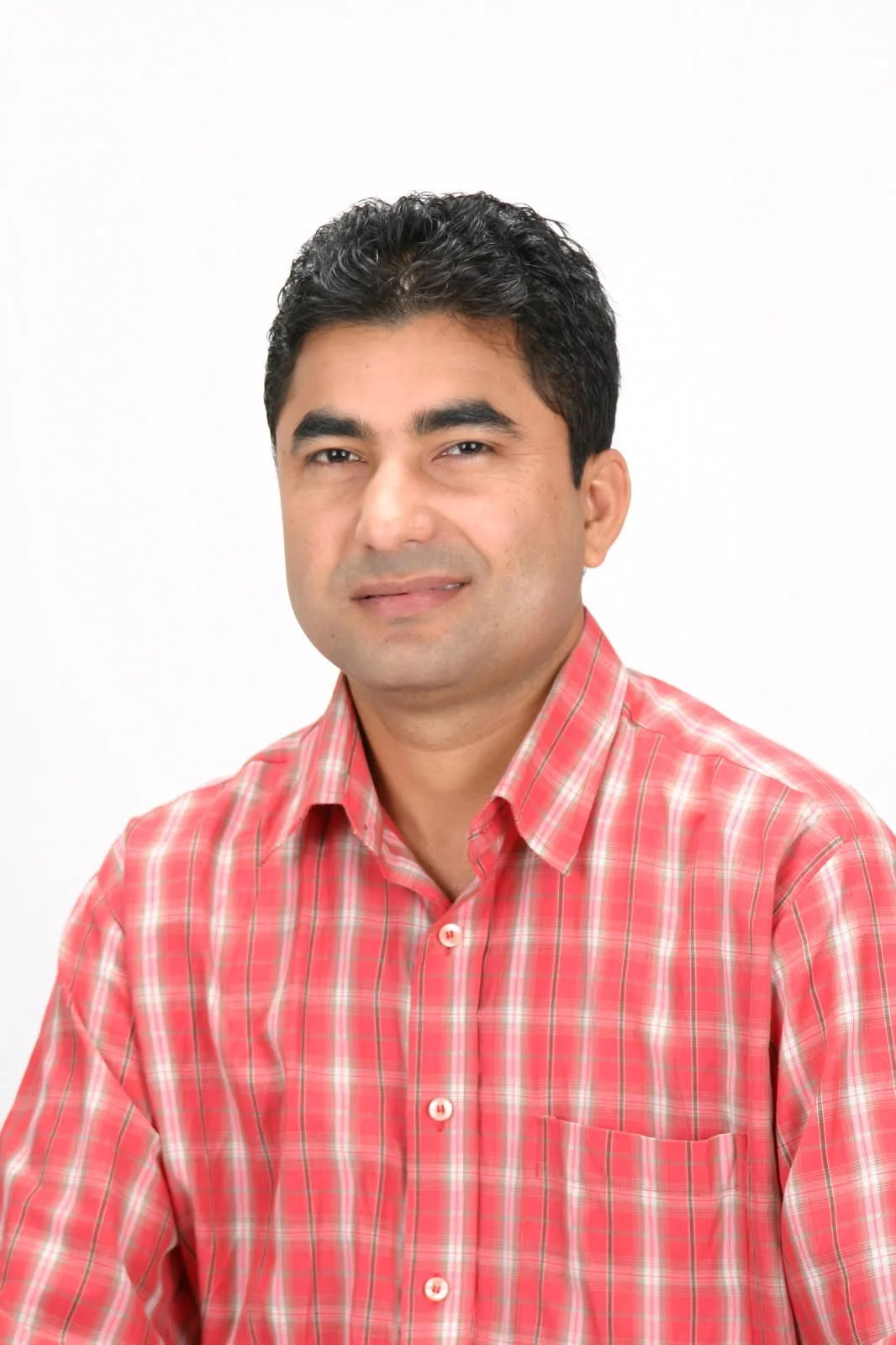 Portrait of a man with dark hair wearing a red plaid shirt against a white background.