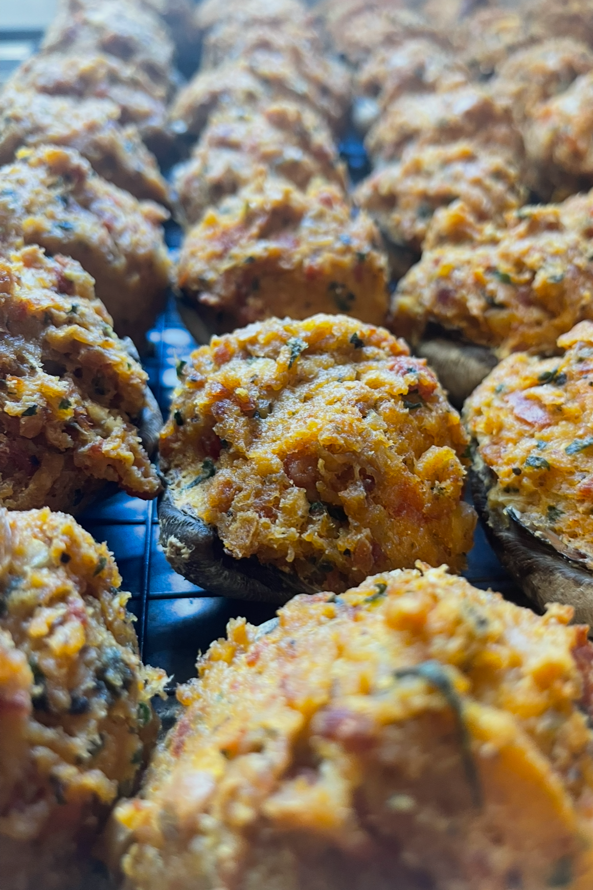 Baked stuffed mushrooms filled with a mixture of herbs, cheese, and possibly vegetables or seafood, resting on a cooling rack.