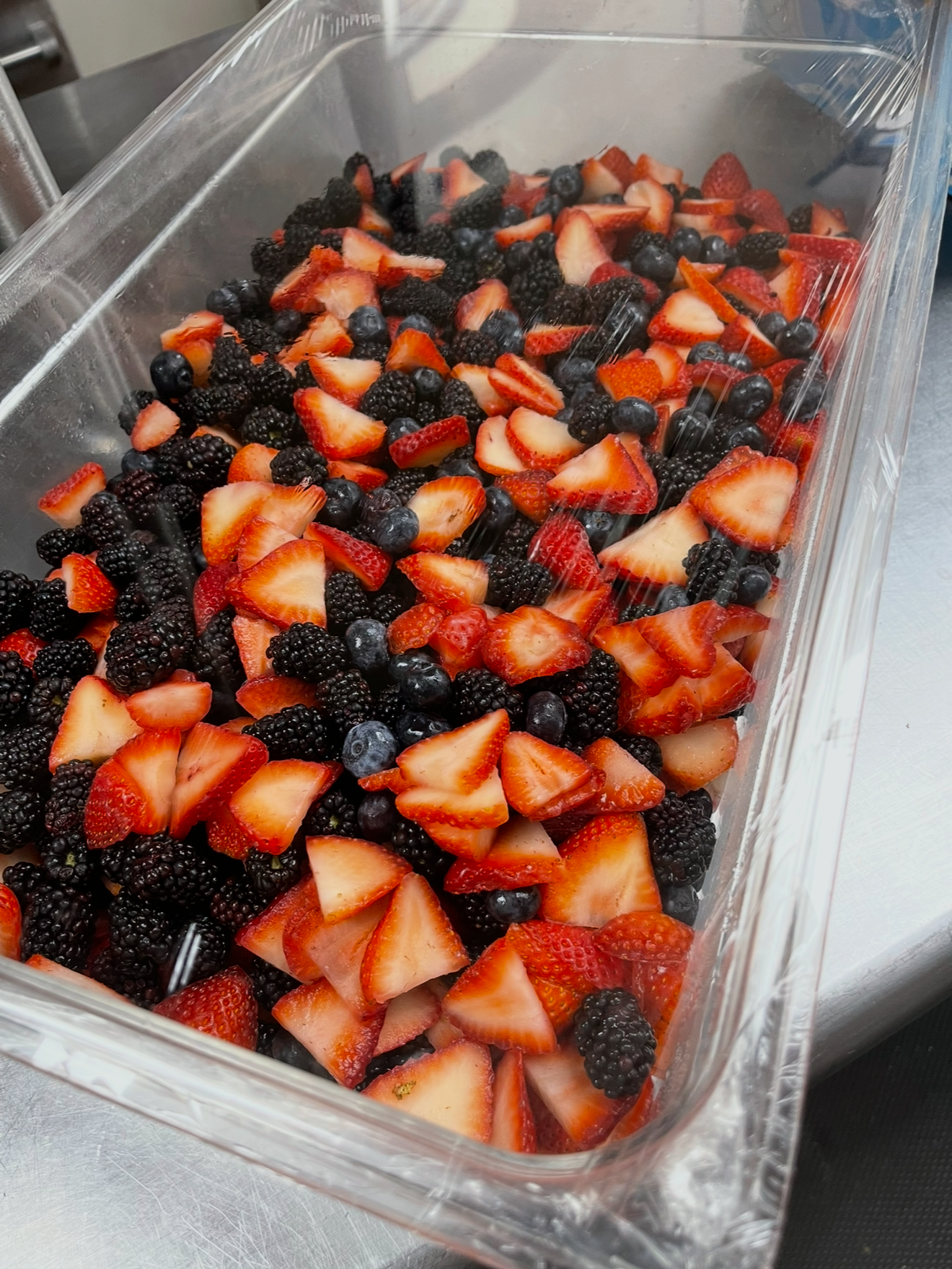 A clear plastic container filled with sliced strawberries, blackberries, and blueberries.