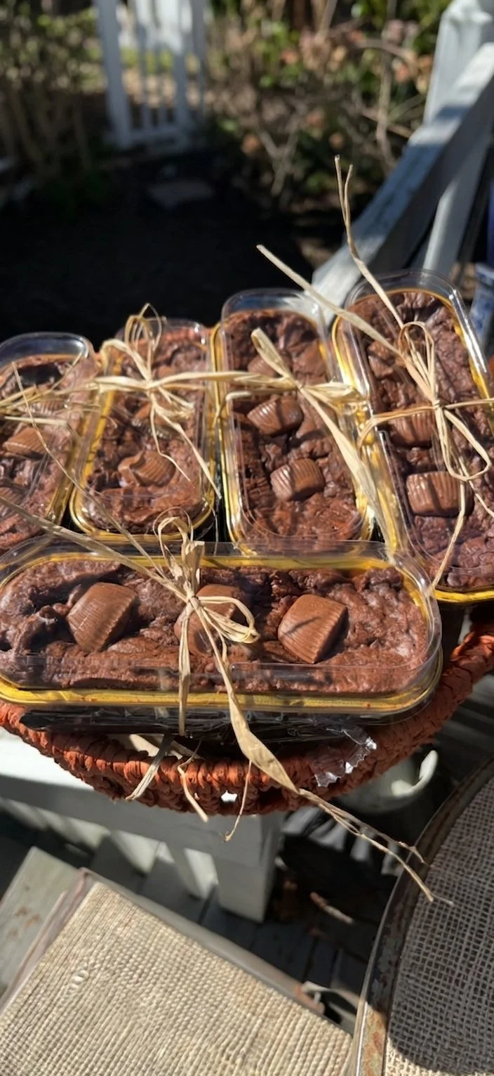 Multiple small plastic containers filled with chocolate pudding topped with chocolate pieces, tied with raffia string, placed outdoors on a woven surface.