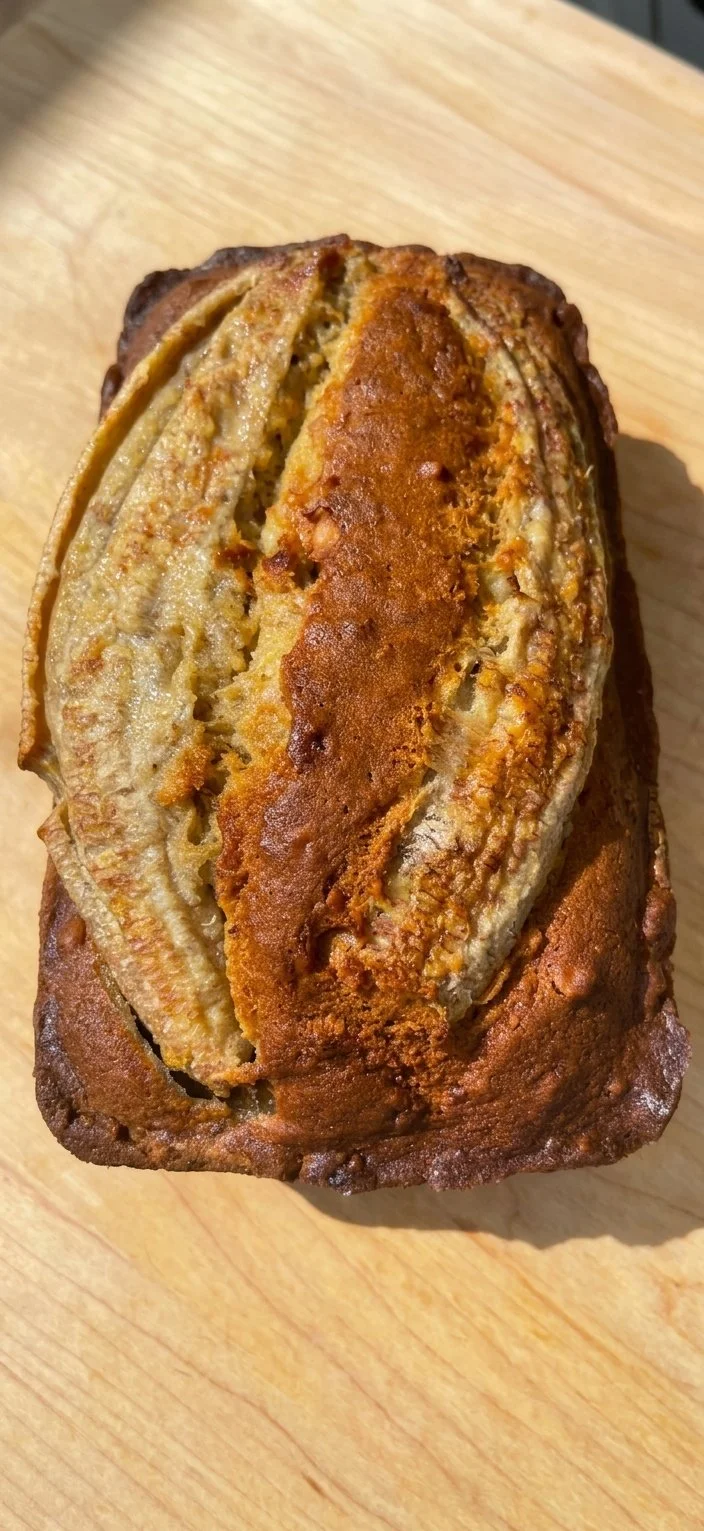 A sliced banana bread loaf with a golden-brown crust on a wooden surface.