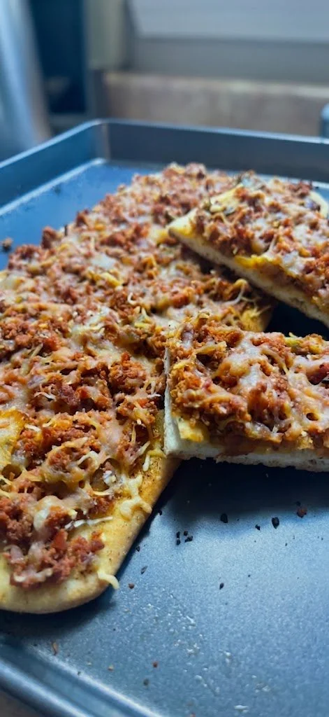 Close-up of a freshly baked meat pizza on a metal tray, with one slice slightly removed.